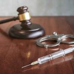 ‘Lindsay Clancy Should Be Dead Too’ Congresswoman Says Syringe beside handcuffs and a judge's gavel on a wooden table