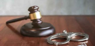 Syringe beside handcuffs and a judge's gavel on a wooden table