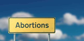 Yellow road sign with the word abortions against a blue sky
