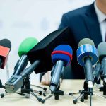 Finger-Pointing Showdown: Jeffries vs. Lawler microphones clustered on a table at a press conference
