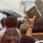 Hand holding a Bible in a crowded church service