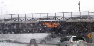 cars driving on snowy highway under bridge during winter storm