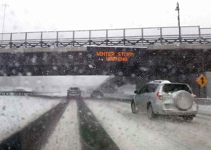 cars driving on snowy highway under bridge during winter storm