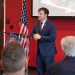 FBI Raids Eric Swalwell’s Home, Seizes Electronics Speaker in a navy suit addressing an audience at a podium