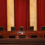 Closed-Door Showdown Over Epstein Insider Empty courtroom bench with red curtains and leather chairs