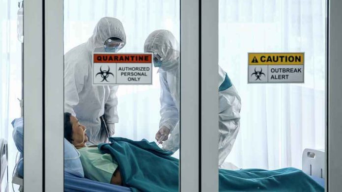 Healthcare workers in hazmat suits treat a patient in a quarantine room