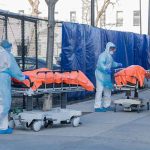 Ebola Surge Outruns Doctors Healthcare workers in PPE move covered stretchers outside a facility