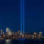 City skyline at night with twin blue light beams rising into the sky