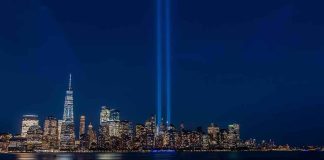 City skyline at night with twin blue light beams rising into the sky