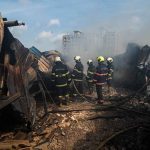 Tanker Near Flames — Laurel Plant Evacuated Firefighters amid twisted metal and smoke at a disaster site