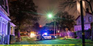 Police car blocks residential street at night behind caution tape