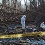 .223 Casing Exposed The Butcher Baker forensic investigators in hazmat suits at a taped-off woodland scene