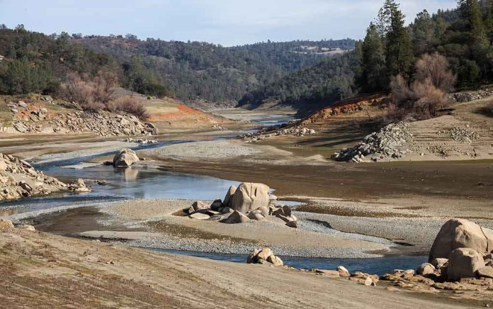Drought-exposed riverbed with scattered boulders and low water