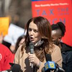 California Targets Fortunes — Lawsuits Locked And Loaded Woman speaking into a microphone at a rally