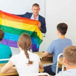 Court Slams Pride Flags In Classrooms Teacher holding a rainbow pride flag in front of students