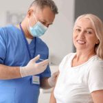 AI Vaccine Hype Outruns The Data Smiling woman receiving a vaccination from a healthcare worker
