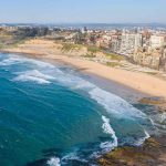 Kamala’s $8M Hideaway Triggers Fury Aerial view of a coastal city beach with waves and rocky shoreline