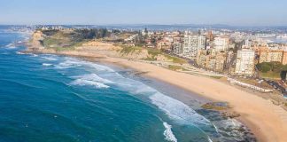 Aerial view of a coastal city beach with waves and rocky shoreline