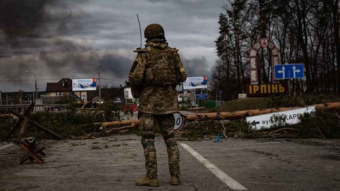 Soldier in camouflage stands at roadblock with smoke in the distance