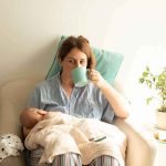 Lindsay Clancy Says ‘A Voice’ Told Her to Kill Her Kids Mother nursing baby while drinking from a mug in a cozy chair