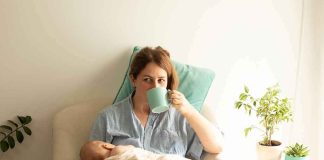 Mother nursing baby while drinking from a mug in a cozy chair