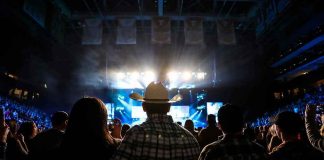 Cowboy-hatted man watches a concert in a packed arena