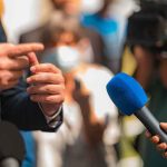 Dem Staffer’s Attack on Nick Shirley BACKFIRES Spectacularly Person in suit speaking to reporters with microphones