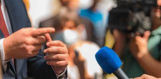 Person in suit speaking to reporters with microphones