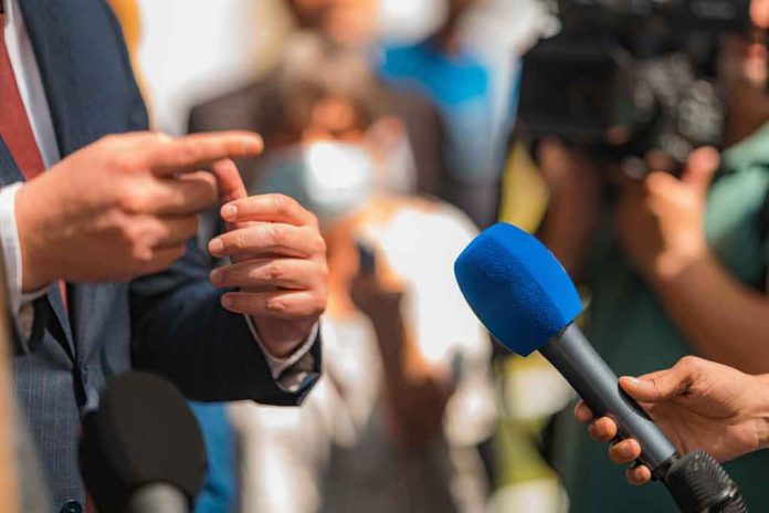 shutterstock_2168392341 Person in suit speaking to reporters with microphones