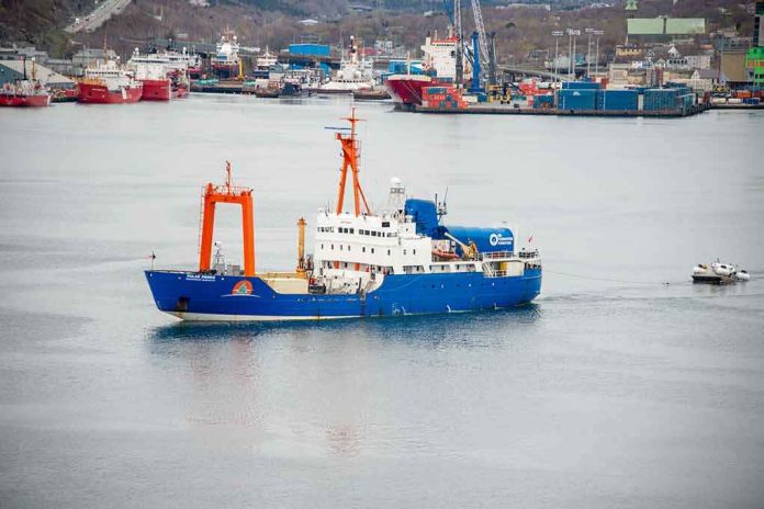 Blue research vessel in harbor with orange cranes