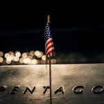 Pentagon Death Toll Vanishes Overnight Small American flag on a memorial with bokeh lights at night