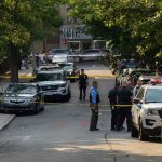 Police officers secure a residential street with patrol cars and yellow tape