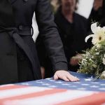 98-Year-Old Vet’s Funeral Shocks Town Mourner rests hand on flag-draped casket with flower arrangement