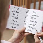 Hands holding a notebook with baby name lists near a crib