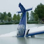 A submerged airplane partially in a lake with trees in the background