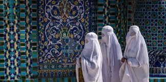 Three women in white veils walking past ornate blue tilework