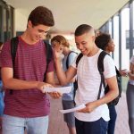 Schools Ban Metal Bottles After Brutal Fights Two students smiling and comparing papers in a school hallway