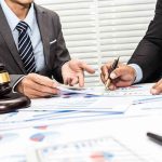Two businesspeople in suits reviewing charts at a desk with a gavel