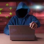 US Says Stolen Google SECRETS Landed in China Hooded figure using a laptop with red cybersecurity graphics