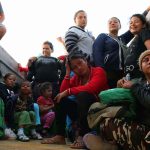 Migrant CARAVAN Is Counting on Democrats Christian Jones among a seated group of people in a crowded outdoor area