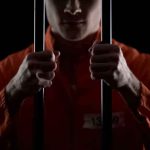 How Inmates Harassed VICTIMS From Behind Bars Prisoner in orange jumpsuit gripping jail bars