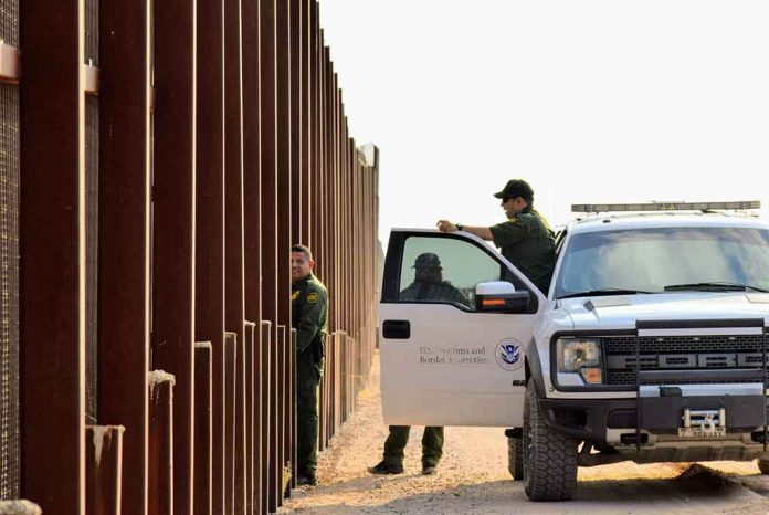 Border patrol agents near a tall fence and a marked pickup truck